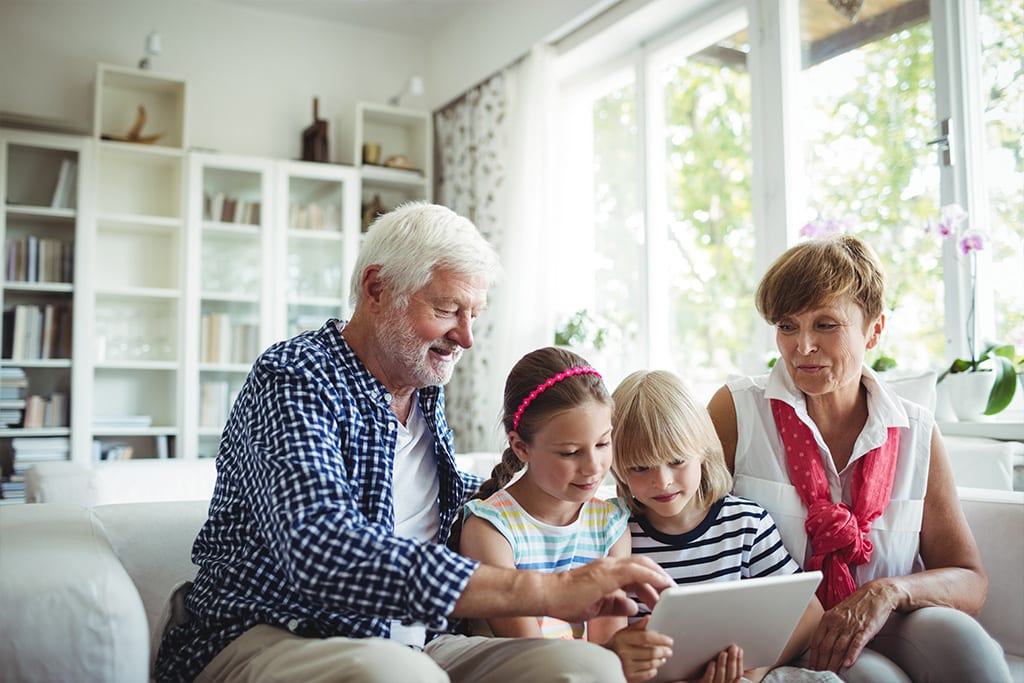 Grandparents using a tablet device with their two school-age grandchildren