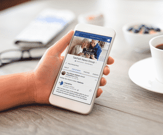 Close up of someone holding a smart phone looking at Lingraphica's TalkPath News Facebook Group page