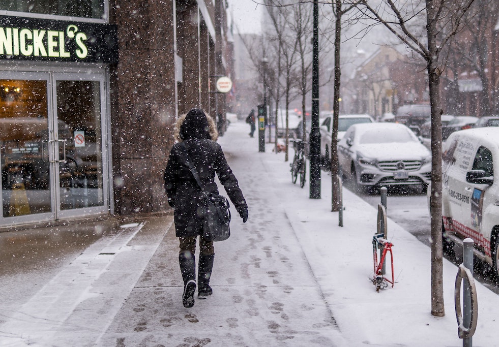 person walking down snowy sidewalk in city