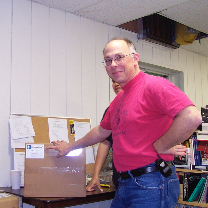 Photo of Robert Gonsalves standing beside the first Lingraphica device, boxed and ready for shipment.