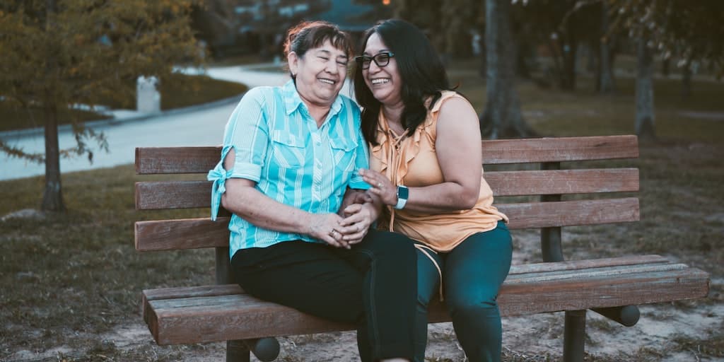 woman and adult daughter sitting and embracing with smiles on a bench