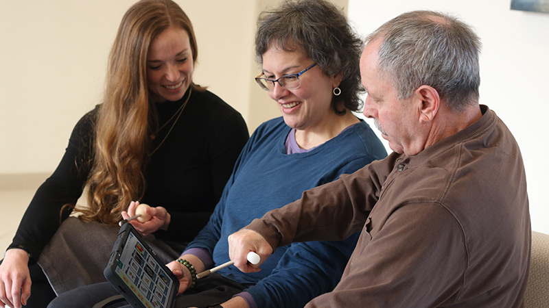 Photo of a couple using a TouchTalk device with an adaptive stylus with their speech therapist.