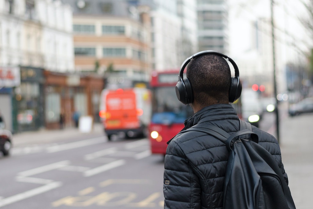 man with back to camera wearing headphones on city street