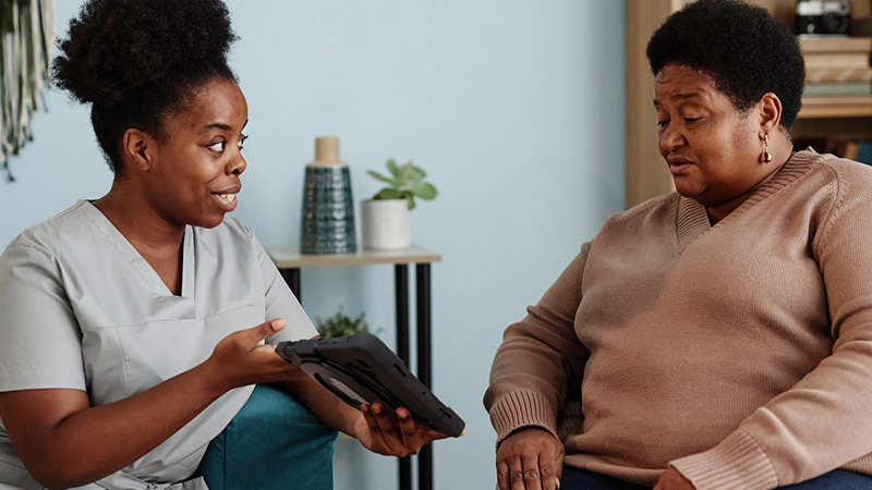 Photo of a home health SLP showing a TouchTalk AAC device to a client.