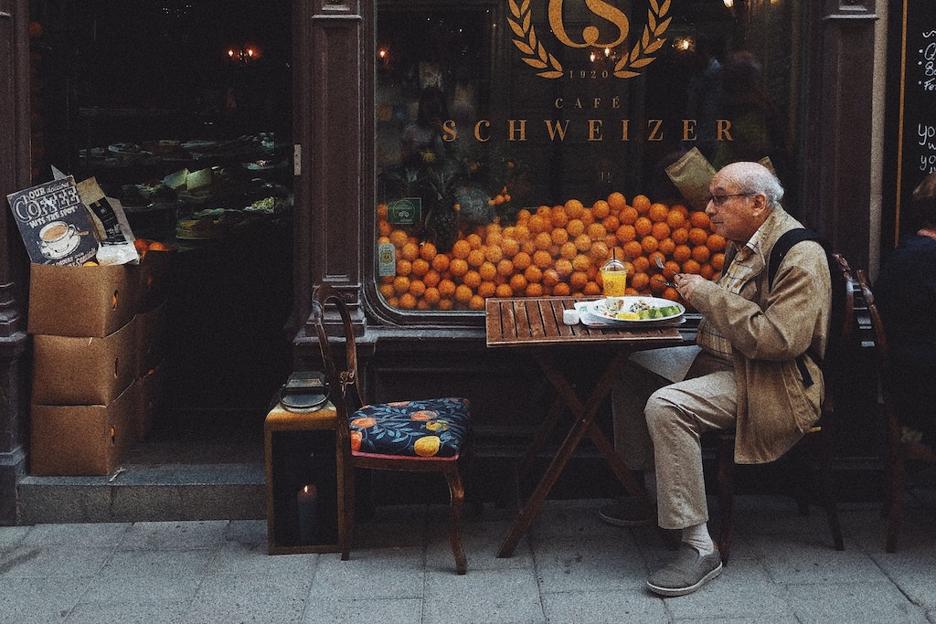 man sitting at sidewalk cafe table in front of window full of oranges