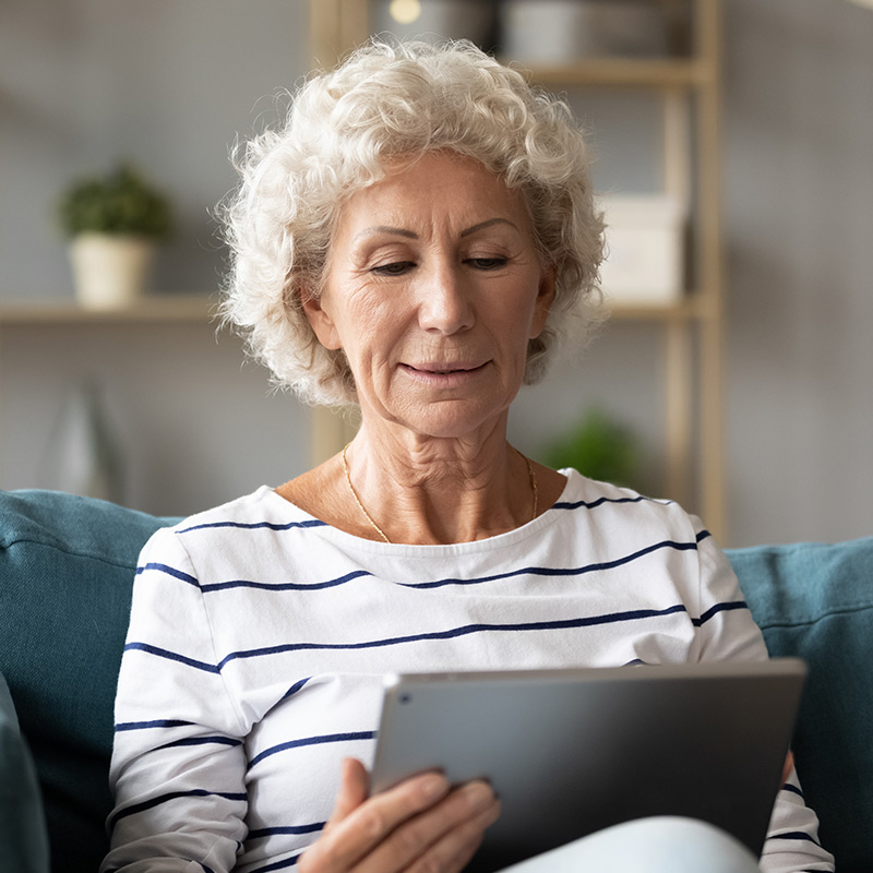 Photo of woman using a tablet device at home on her couch.