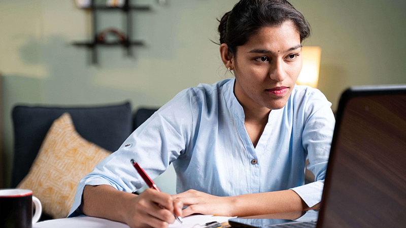 Photo of a woman working on her laptop and taking notes.