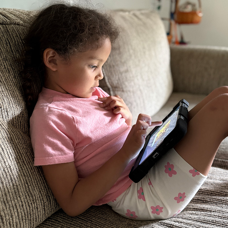 Young girl using a MiniTalk AAC device on her couch at home.